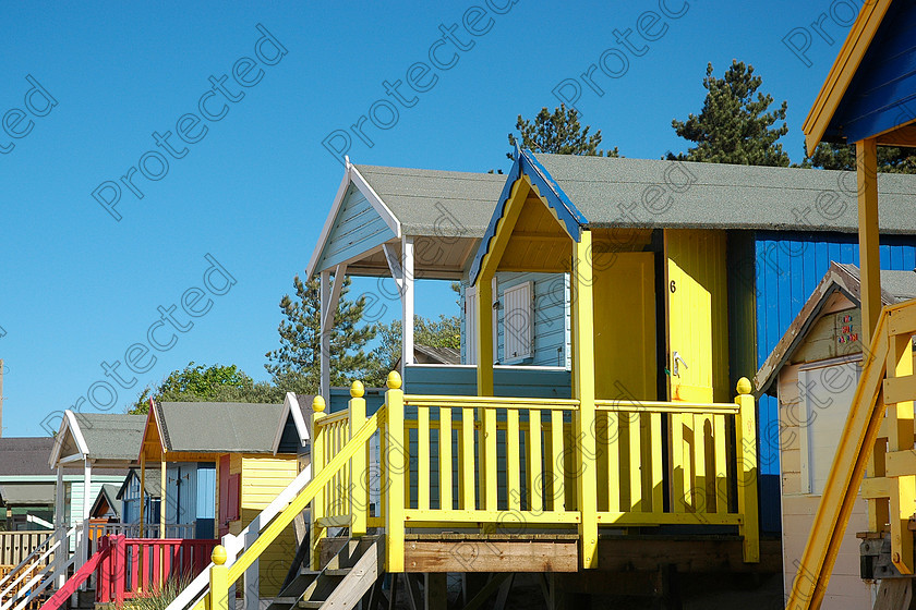 UK Norfolk DSC 0343 
 Colourful beach huts against blue sky 
 Keywords: beach, beachfront, blue, britain, building, coast, color, colorful, england, holiday, house, hut, ocean, relax, resort, roof, rustic, sand, sea, seaside, season, shelter, sky, summer, summertime, sun, sunny, sunshine, tourism, traditional, travel, vacation, warm, waterfront, wooden, yellow